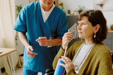 Senior woman using breathing apparatus while receiving assistance from healthcare professional in home environment