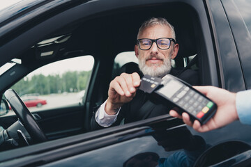 Senior businessman in a car using contactless payment at a parking lot, highlighting technology and...