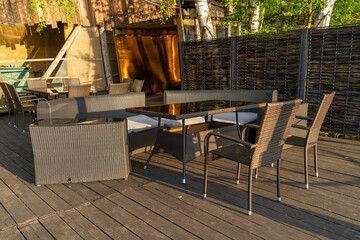 Cozy outdoor seating area features wicker furniture arranged on wooden decking, illuminated by warm golden sunlight in a peaceful setting