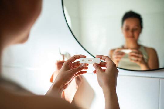 Shocked woman holding positive pregnancy test in bathroom