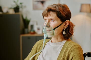 Elderly woman wearing oxygen mask sitting in a cozy home setting, surrounded by household items and...