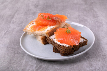 Slices of smoked trout on wheat and rye bread with cream cheese on a ceramic plate