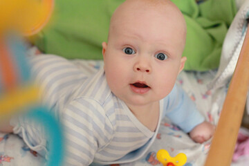 5 month old baby in a blue bodysuit lies in a crib and looks at the camera, close-up newborn