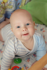 5 month old baby in a blue bodysuit lies in a crib and looks at the camera, close-up