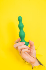 Female hand with green anal plug sticking out of yellow paper background.
