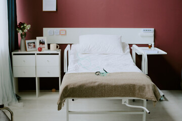 Empty hospital bed with medical equipment and a nightstand in a clean, well-lit room with beige walls, displaying a serene and orderly atmosphere