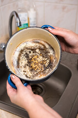 A pair of hands holding a pot with burnt food residue over a sink. Perfect for depicting kitchen cleanup tasks and household chores