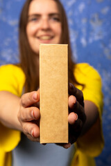 A person in yellow clothing holding a plain, rectangular box towards the camera, with a blue...