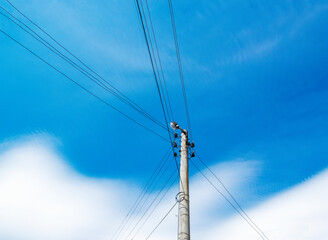 Fototapeta premium Concrete electric pole with a lamp and cables against sunny May sky with clouds, low-angle partial view from a village in North Bulgaria