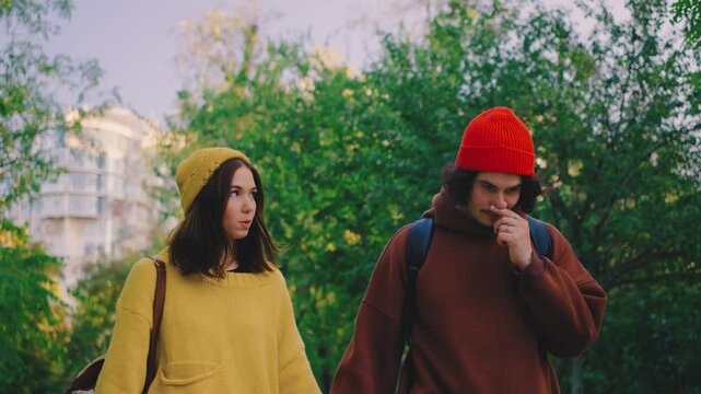 A couple walks hand in hand through the park, but their expressions show tension and disagreement. They are upset, reflecting the conflict between them in the peaceful setting