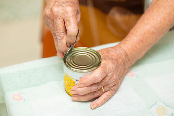 Close up em mãos de uma cozinheira abrindo uma lata de milho em conserva sobre uma mesa de cozinha.