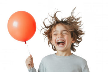 A young boy with tousled hair laughs joyfully while holding a bright orange balloon. His carefree expression radiates happiness, creating a light-hearted atmosphere.