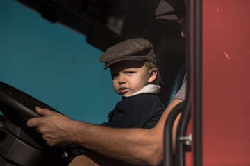 A Cute little boy driving is fathers truck with Dad