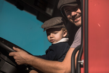 A Cute little boy driving is fathers truck with Dad