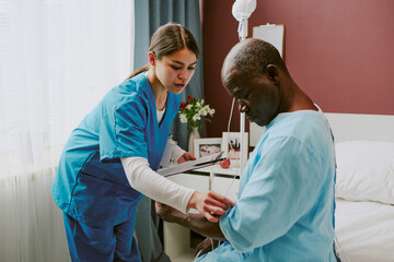 Nurse providing medical care to senior black patient sitting in hospital room with healing...
