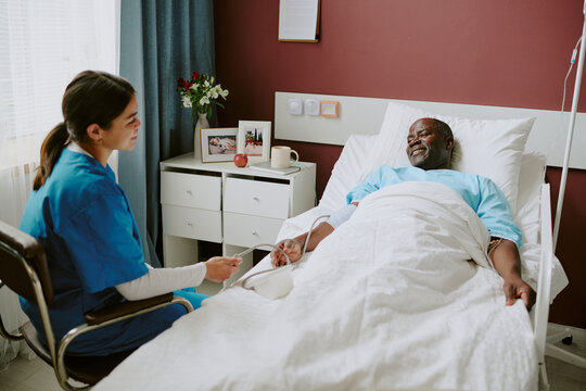 Nurse tending to bedridden patient in hospital room, providing care and compassion, medical equipment and personal items visible around creating a comforting environment