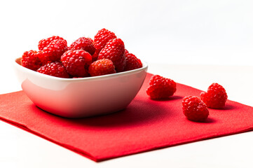 Ripe raspberries in a white bowl, on a red napkin. Raspberry cultivation and use.