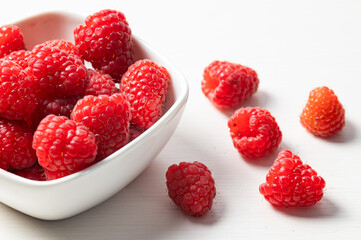 Ripe raspberries in a white bowl, on a red napkin. Raspberry cultivation and use.