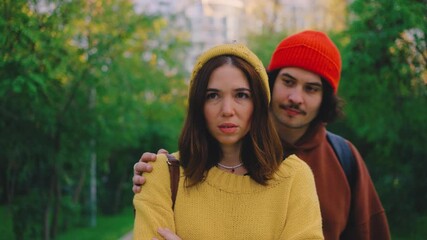 A woman appears sad in the park, her boyfriend approaching to console her with a hug. Despite his care, she walks away, leaving him standing alone. the guy shows her the middle finger in response