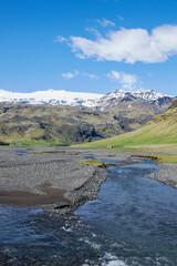 Mountain valley iceland. With river and black rock stones. Green hills and snow mountains. Sunny day with white clouds. Alone in the wilderness scenic background