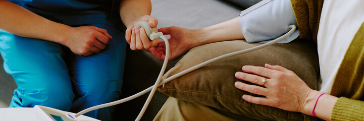 Elderly person receiving blood pressure measurement from healthcare professional using medical device, showcasing medical care and patient interaction during examination