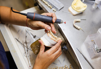 Dental technician shaping prosthetic teeth with rotary tool.