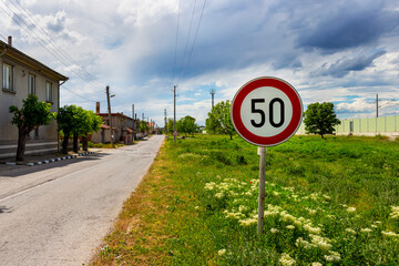 Prohibitory sign Speed limit (50 km/h) at the beginning of the village of Krum, Southern Bulgaria, Haskovo Region under stormy May sky