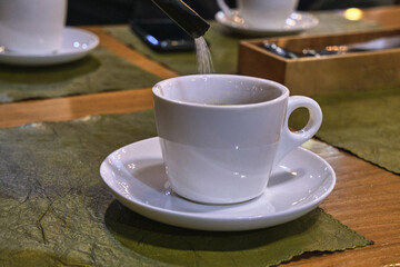 Sugar is pouring from a disposable packet into a cup of coffee.
