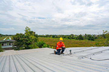 Technician in safety uniform and helmet kneeling on a rooftop, using a drill for precise...