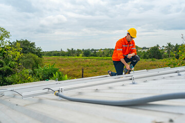 Technician in safety uniform and helmet kneeling on a rooftop, using a drill for precise...