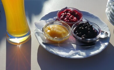 Glass plate with three types of fruit compotes and a glass of beer on the side.