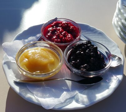 Close-up of three fruit compotes in small glass bowls on a white plate.
