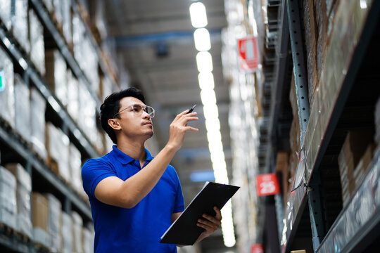 supply chain and logistic network technology concept. Happy Asian worker in blue uniform with clipboard in warehouse. Happy workers in the distribution center. - Powered by Adobe