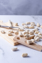 Counter full of gnocchi in preparation with knife, utensil and wooden board.