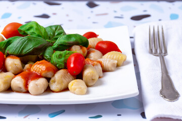 A plate of gnocchi with sauce, tomato and basil leaves.