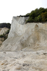 White limestone cliff being eroded by natural elements with plants s at risk of falling from the top