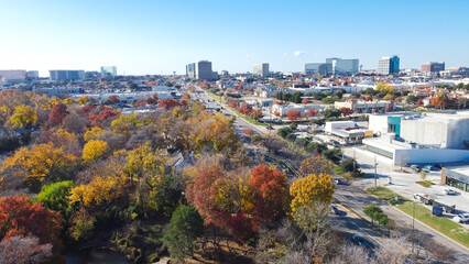 Yellow red orange fall foliage over urban park along Belt Line Road with office buildings, skylines, commercial complex in North Dallas and Addison, sunny clear blue sky, vibrant autumn leaves