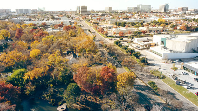 Yellow red orange fall foliage over urban park along Belt Line Road with office buildings, skylines, commercial complex in North Dallas and Addison, sunny clear blue sky, vibrant autumn leaves