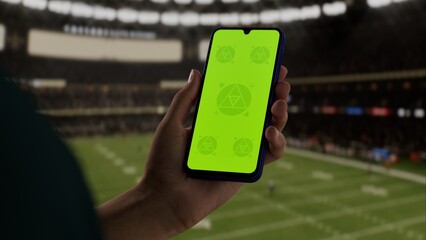 GREEN SCREEN CHROMA KEY A hand holding a phone with a green screen at an American football game in a stadium at night, perfect for showcasing live sports or betting apps