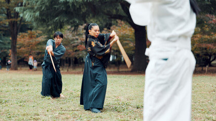 Sword, martial arts and people in outdoor class together for aikido training, fight coaching or samurai challenge in nature. Warrior, Japanese man and woman in park for traditional bokken battle kata