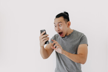 Shock and wow face Asian man in grey t-shirt use smartphone app on white.