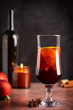 One glass of traditional homemade winter hot red mulled wine drink or spiced grog cocktail made with orange slices, cinnamon and anise served on table with christmas baubles, bottle and candle light