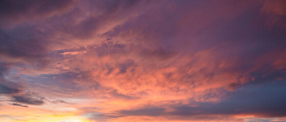 Obraz premium Dramatic sunset sky with vibrant hues of orange, pink, and purple, featuring textured clouds illuminated by fading sunlight, creating a serene atmosphere