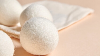 Close-up of soft wool dryer balls placed near a cotton drawstring bag on a beige background....