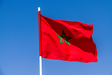 Moroccan flag waving with a green star under a clear blue sky