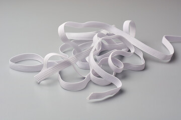 pile of white knitted elastic bands isolated gray background, commonly used in textile industry garments, sportswear and lingerie, soft focus