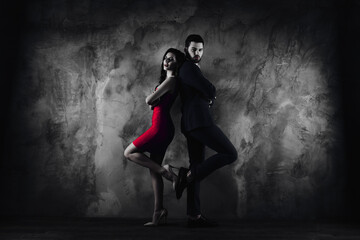 Full size body portrait of attractive couple with crossed arms looking at camera, charming slim lady in purple tight dress gentlemen in tux standing back to back over grey wall