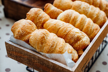 On a beautiful wooden box resting on a table, there is a delightful assortment of freshly baked croissants, ready to be enjoyed with coffee or tea as a perfect snack or breakfast option