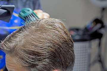 barber blow-dries a teenager's medium-length hair after a haircut. Image and personal style