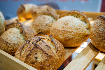 On a sturdy wooden shelf, there rests a beautifully crafted wooden box that is filled to the brim with various delicious and freshly baked bread rolls, waiting to be enjoyed